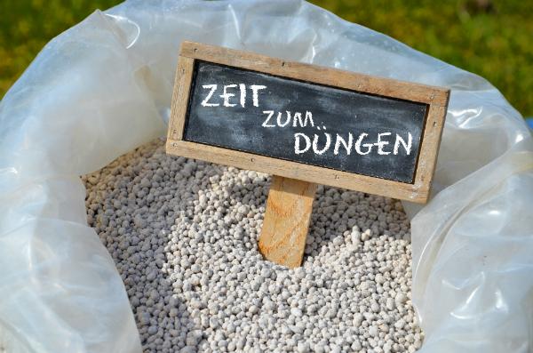 Frühjahrsdüngung Ein Sack mit Rasendünger, der mit einem Schild mit der Aufschrift "Zeit zum Düngen" versehen ist