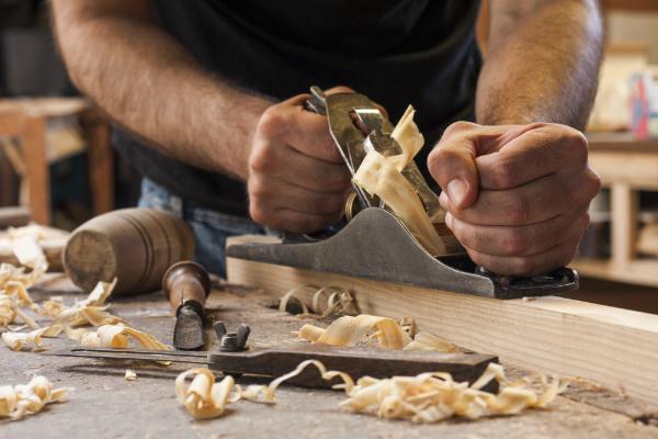 In Schrittstellung neben dem Holz und in langen Zuegen hobeln