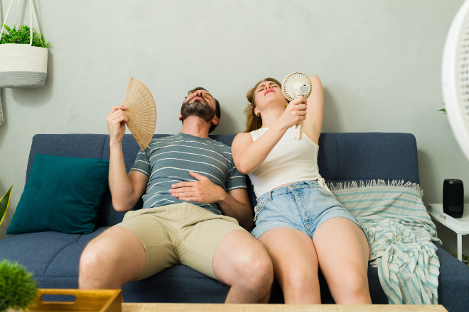 In der Wohnung hat der Sommer nicht nur angenehme Seiten Ein Paar versucht sich auf der Couch bei Sommerhitze mit einem Fächer etwas Kühlung zu verschaffen