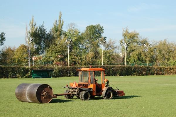 Traktor mit Schwermetallrasenrolle auf Fußballplatz