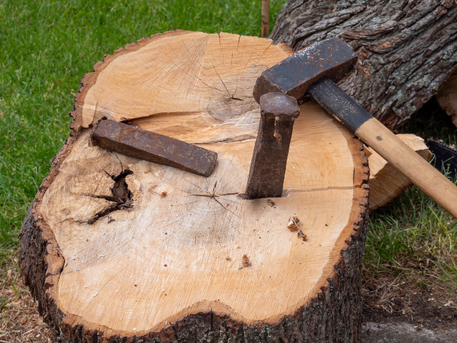 Auch ein Spaltkeil leiste gute Dienste Auf einem großen Holzstück liegt ein Hammer und ein Spaltkeil