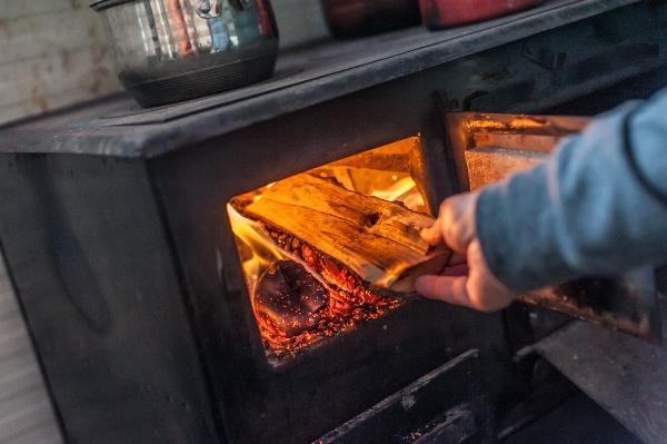 Mann legt Holz beim Holzherd nach