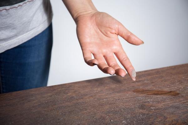 Eine Frau wischt mit dem Finger über eine staubige Tischplatte. An ihrem Finger haftet jede Menge Staub. Gegen stickige Luft 