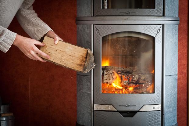 Frau legt Holzscheit in den Kamin