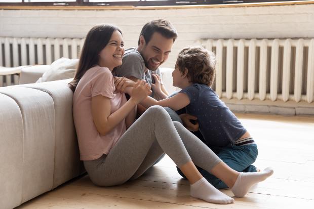 Junge Familie (Vater, Mutter, Kind) sitzt vor der Heizung