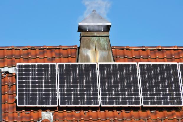 Ein rauchender Schornstein, vor dem eine Photovoltaikanlage zu sehen ist Wärmewende