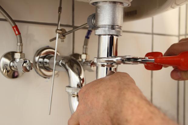 Ein Mann schraubt die Verbindung zwischen Waschbecken und Siphon auf Abfluss am Waschbecken wechseln