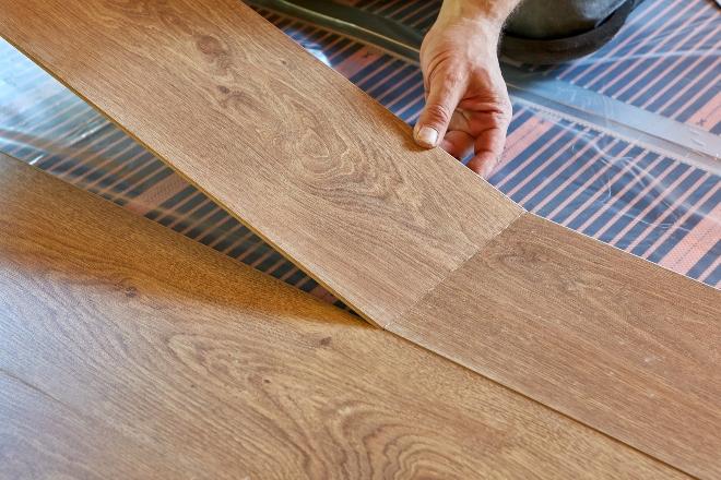 Mann legt Laminat auf Fußbodenheizung - Wandheizung oder Fußbodenheizung bieten jeweils eigene Vorteile