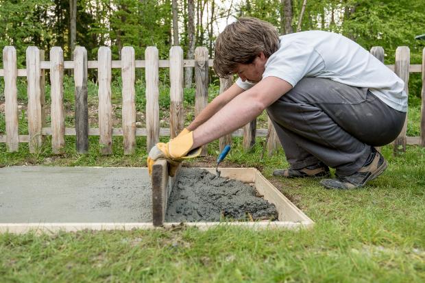 Mann baut Fundament im Garten - Geräteschuppen einrichten