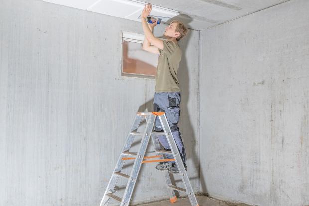 Mann installiert Dämmung an Kellerdecke - Tipps für den Kellerausbau