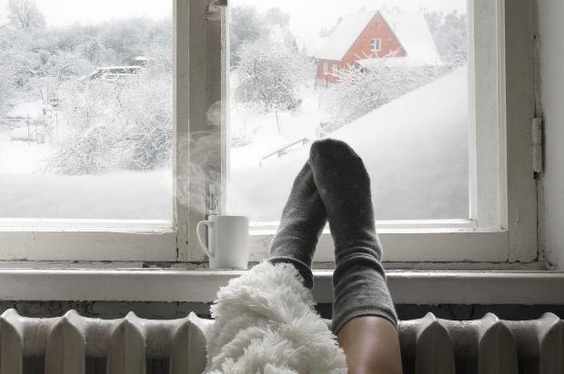 Jemand legt im Winter seine Füße auf die Heizung vor dem Fenster