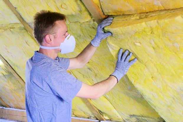 Mann dämmt Dachboden - durch Dämmung Energiekosten sparen