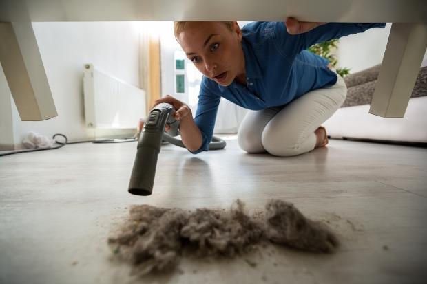 Frau reinigt Staub unter einem Tisch