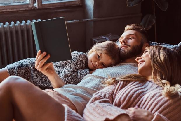 Junge Familie auf dem Bett liest ein Buch zusammen