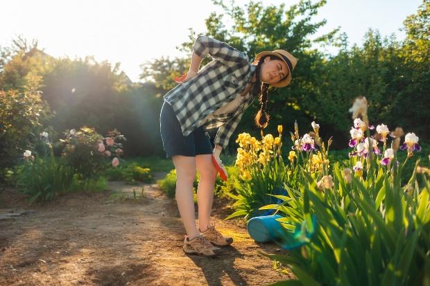 Junge Frau mit gekrümmtem Rücken beim gießen mit Gießkanne - Beetbewässerung auf die klassische Art