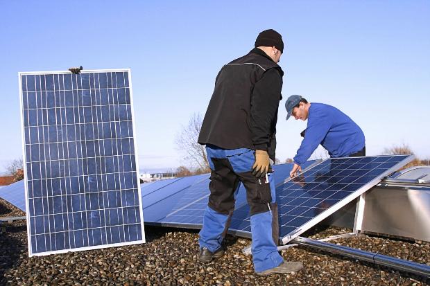 Zwei Arbeiter montieren auf einem Flachdach Solarkollektoren