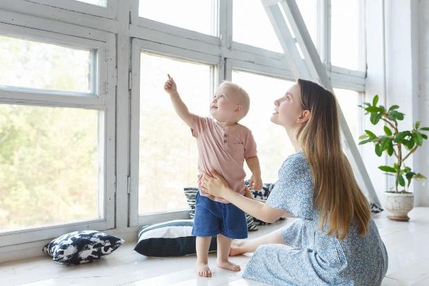 Mutter mit Kind sitzen im hellen Haus, vor vielen Fenstern