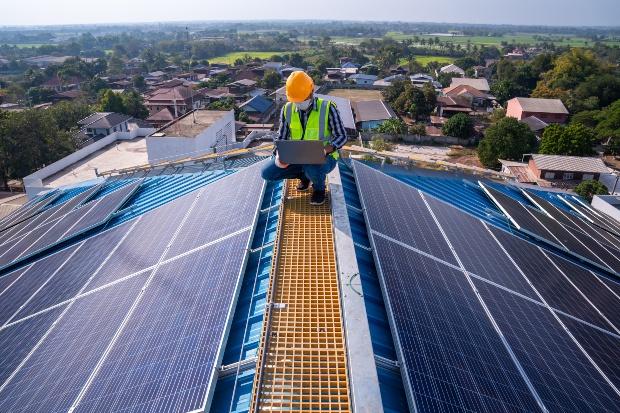 Mann steht auf einem Hausdach, kontrolliert die Solaranalage - Solarpflicht könnte kommen