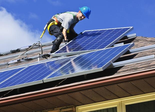 Ein Handwerker installiert ein Solarmodul auf einem Hausdach