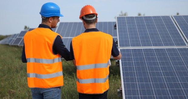 Zwei Arbeiter stehen vor einer großen, in der Fläche aufgebauten Photovoltaikanlage Geschichte der Photovoltaik