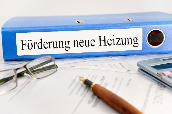 Auf einem Schreibtisch liegt ein Ordner mit der Aufschrift: "Förderung neue Heizung" Auslaufmodell Gasheizung