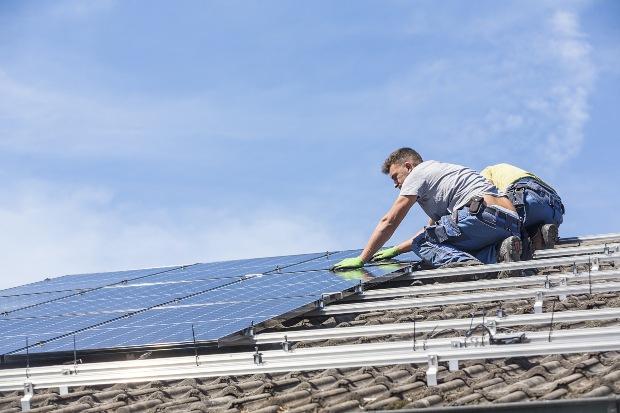 Männer installieren Solaranlage auf Häuserdach