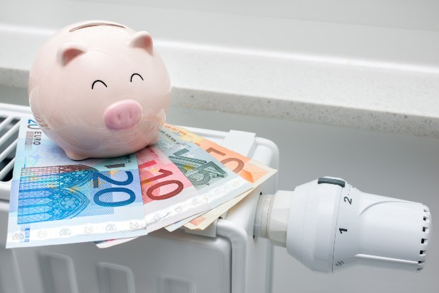 Sparschwein und Geldscheine auf einer Heizung - Warmwasserkosten senken