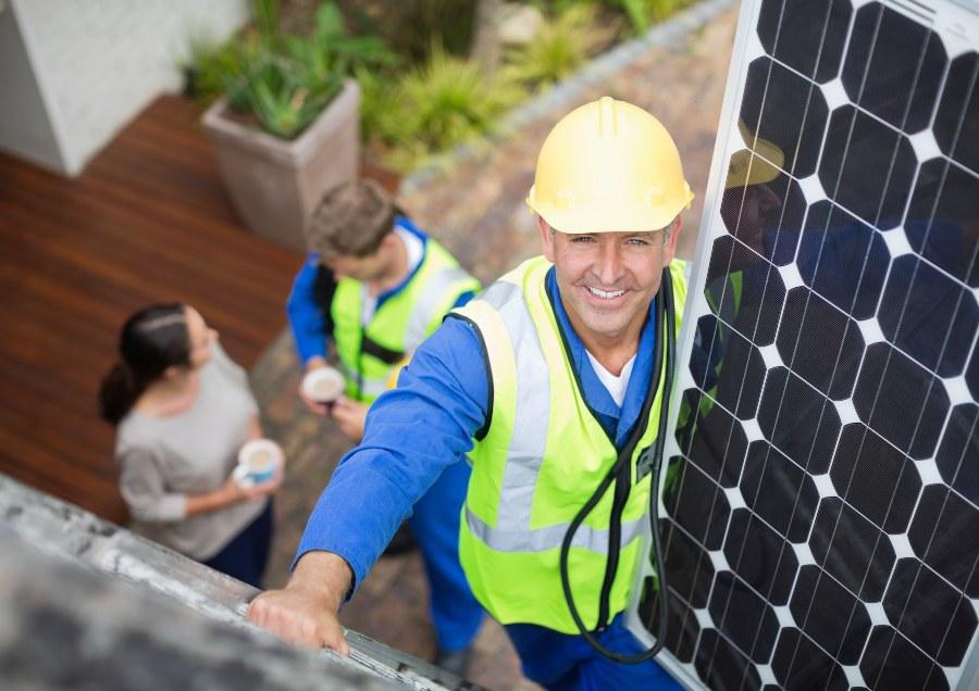 Handwerker trägt Solarpanel auf ein Hausdach