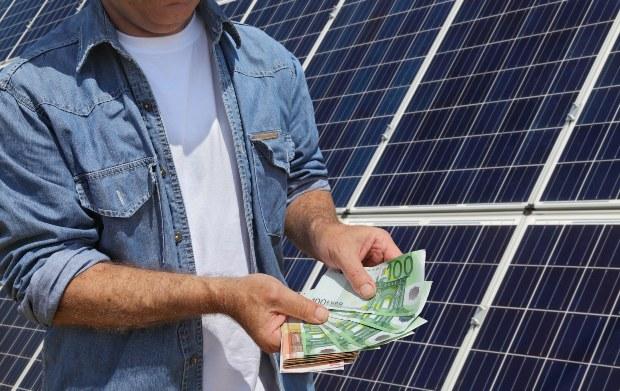 Mann mit Geldscheinen vor Photovoltaik-Anlage 