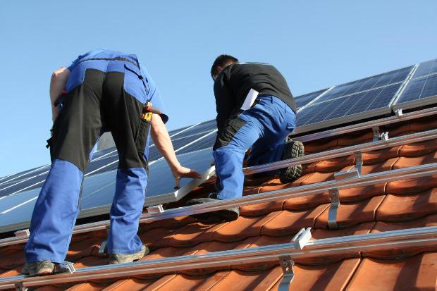 Zwei Arbeiter montieren eine Solaranlage auf einem Giebeldach