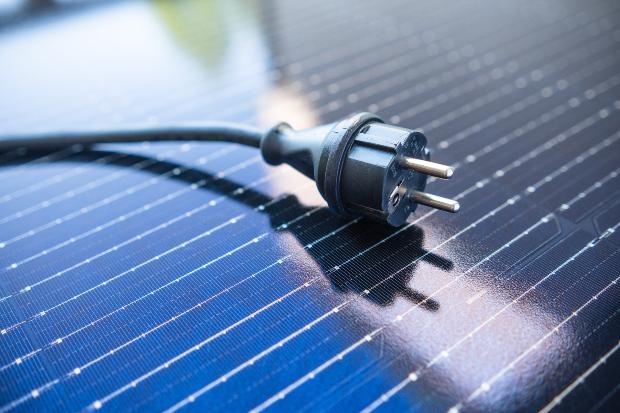 Ein Elektro-Stecker liegt auf einem Solarzellen-Panel